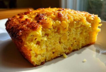 Close-up of a moist slice of cornbread casserole showing visible corn kernels and a golden-brown crust.