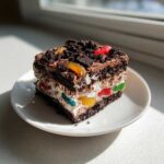 A layered slice of amazing dirt cake featuring chocolate layers, white cream, and colorful gummy worms, topped with cookie crumbs.