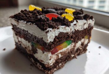A layered slice of amazing dirt cake featuring chocolate cake, cream, and colorful gummy worms peeking out.