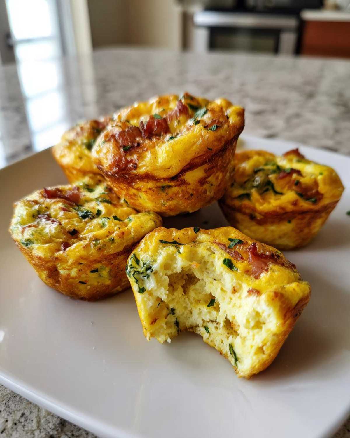 Four golden brown egg bites, one with a bite taken out, showing the fluffy interior and bacon pieces.