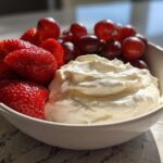 A white bowl filled with creamy fruit dip, fresh strawberries, and red grapes, perfect for dipping.