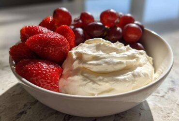 A white bowl filled with creamy fruit dip, fresh strawberries, and red grapes, perfect for dipping.