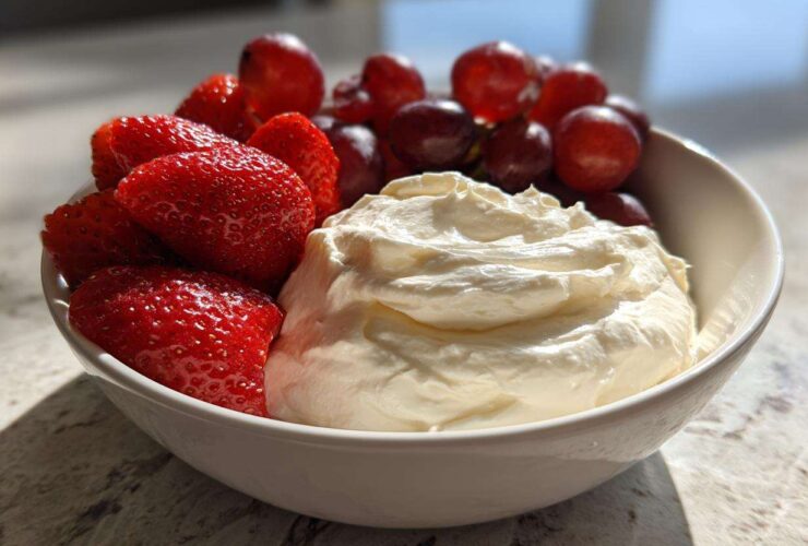 A white bowl filled with creamy fruit dip, fresh strawberries, and red grapes, perfect for dipping.