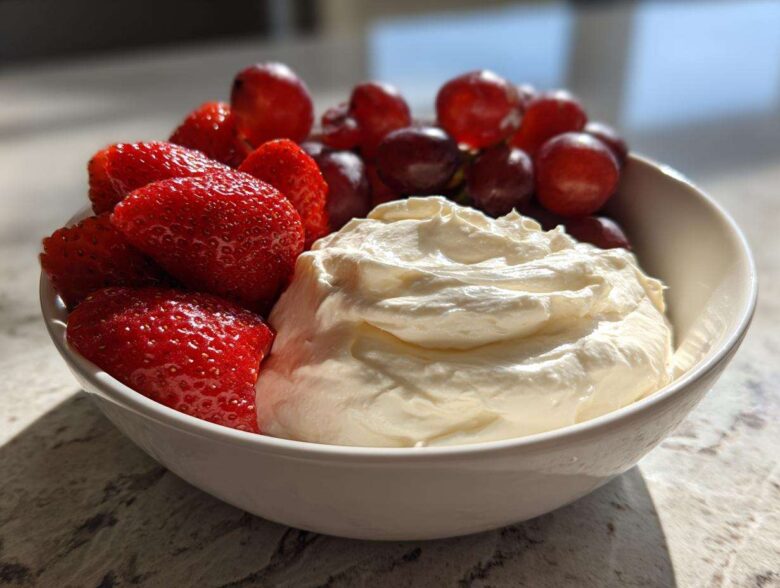 A white bowl filled with creamy fruit dip, fresh strawberries, and red grapes, perfect for dipping.