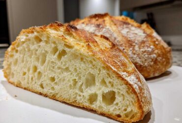 Close-up of a freshly baked Italian bread loaf, showing the open, airy crumb structure and golden, flour-dusted crust.