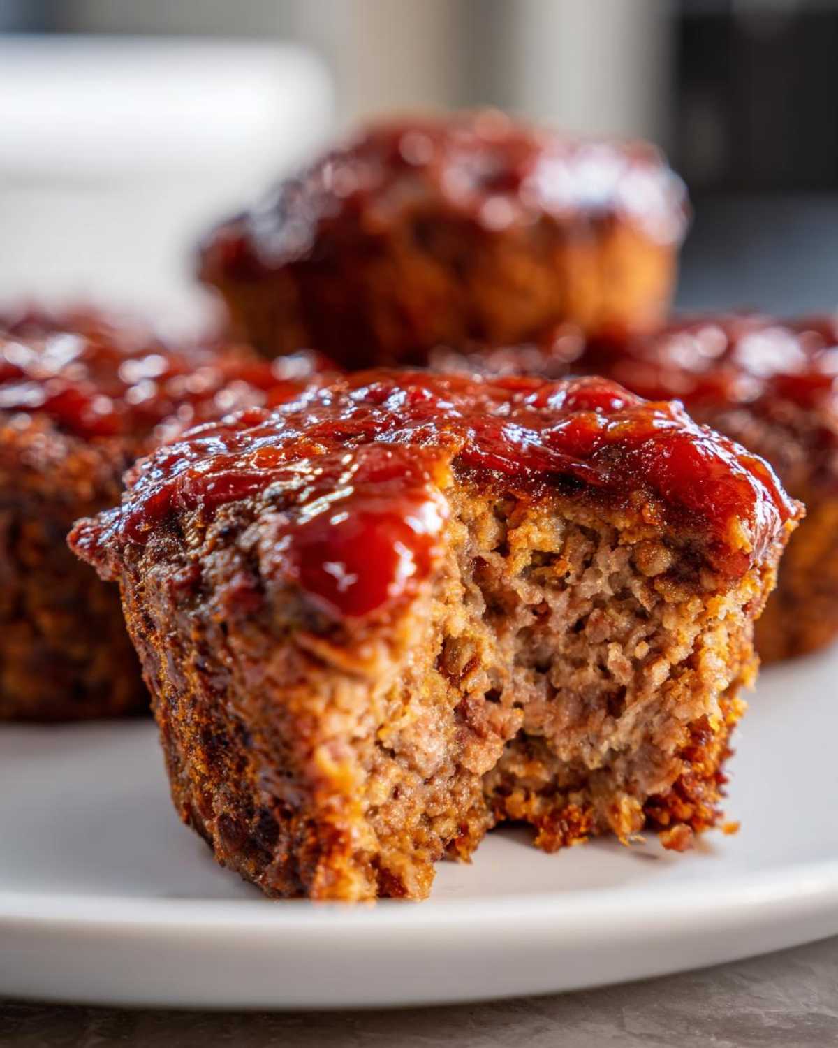 Close-up of a moist mini meatloaf topped with shiny ketchup glaze, showing the texture inside after a bite was taken.