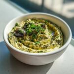 Close-up of a creamy, green-flecked olive dip topped with whole olives and fresh parsley.