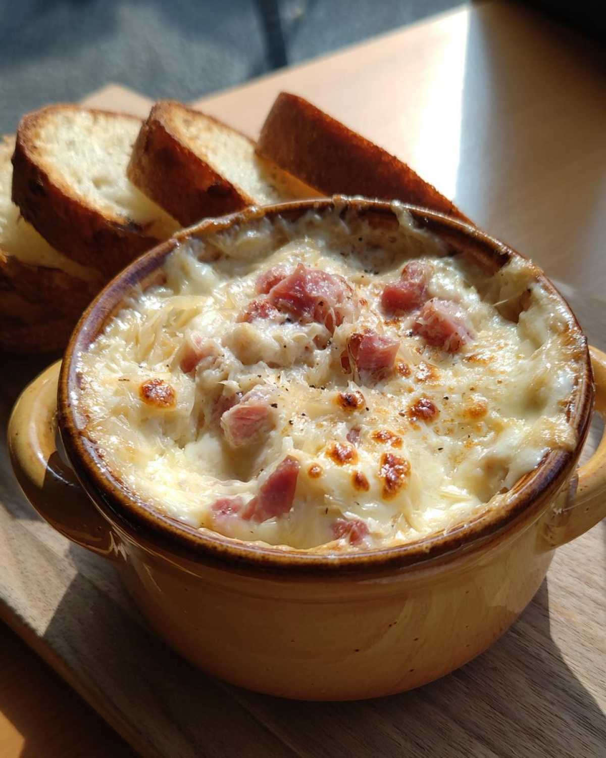 Close-up of a hot, cheesy reuben dip topped with chopped meat, served with slices of toasted baguette.
