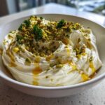 A white bowl filled with creamy ricotta dip, drizzled with honey and topped with chopped pistachios and parsley.
