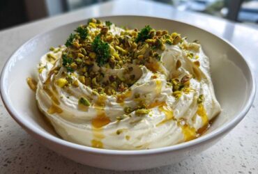 A white bowl filled with creamy ricotta dip, drizzled with honey and topped with chopped pistachios and parsley.