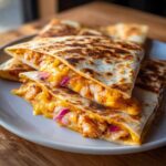 Close-up of stacked, grilled shrimp quesadilla wedges oozing melted cheese, shrimp, and red onions.