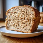 A thick slice of amazing whole wheat bread showing a soft, even crumb texture on a light plate.
