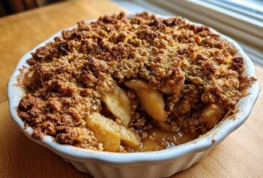 Close-up of a golden brown, bubbling apple crisp recipe baked in a white dish.