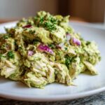 A close-up of a serving of creamy avocado chicken salad mixed with chunks of red onion and fresh herbs.