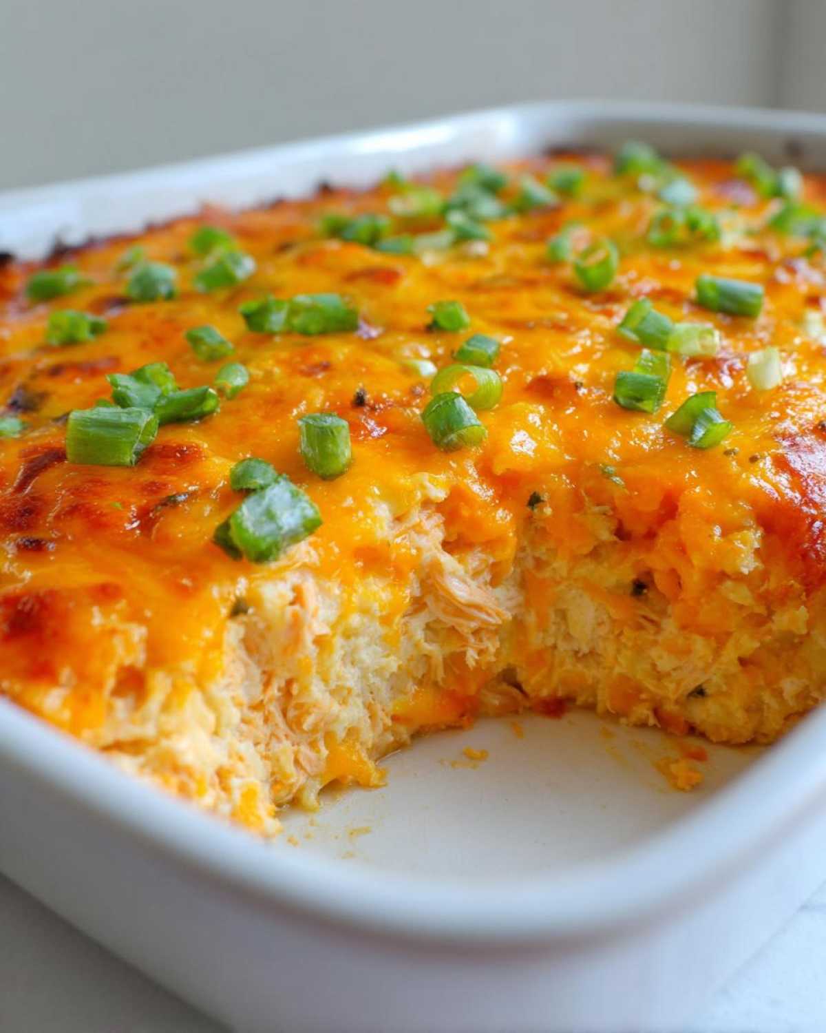 Close-up of baked Buffalo chicken dip in a white dish, showing melted orange cheese and chopped green onions.