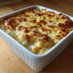 A square white baking dish filled with hot, creamy baked corn dip topped with bubbly, golden-brown melted cheese.