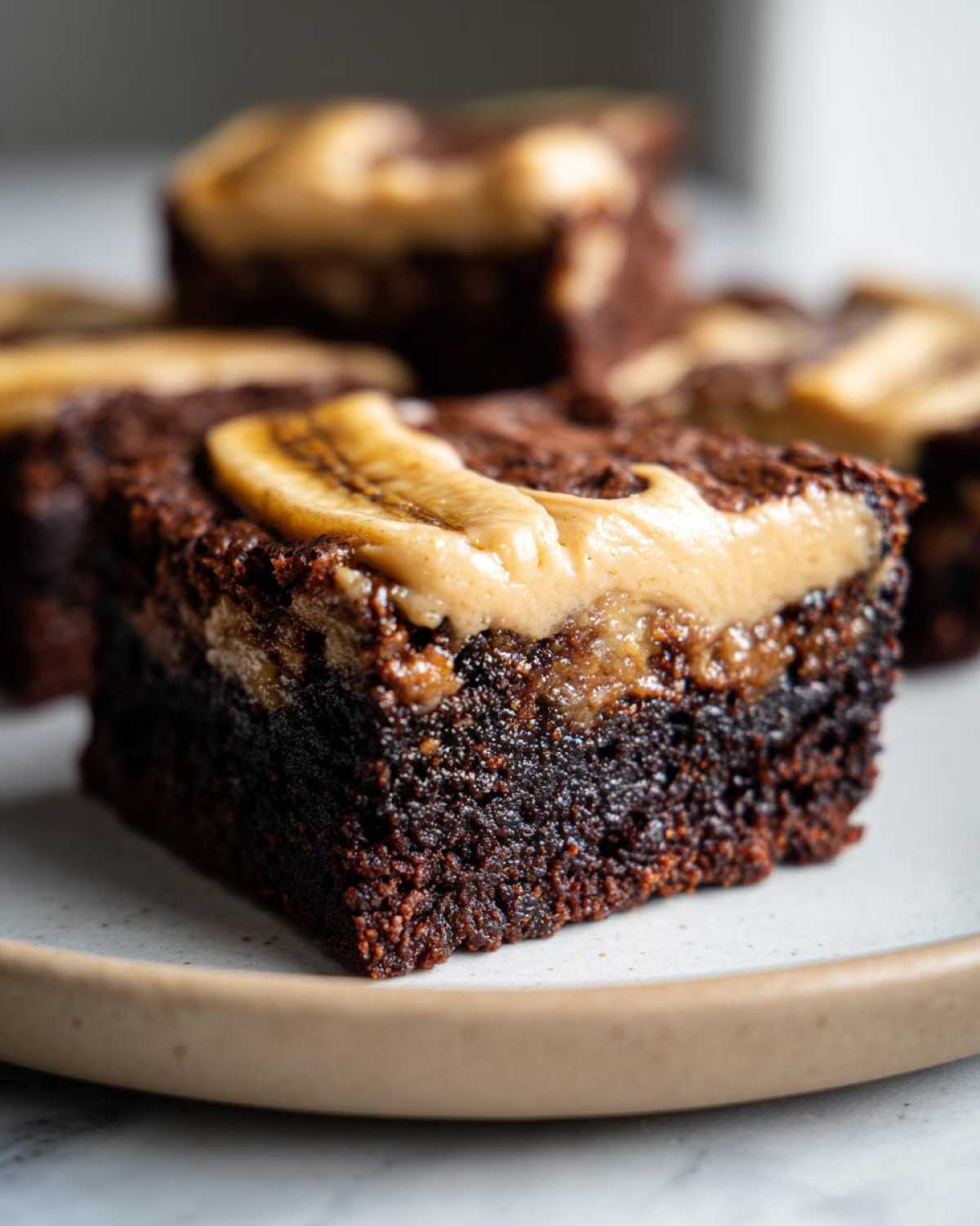 A rich, fudgy square of banana bread brownies topped with a swirl of peanut butter and a slice of banana.