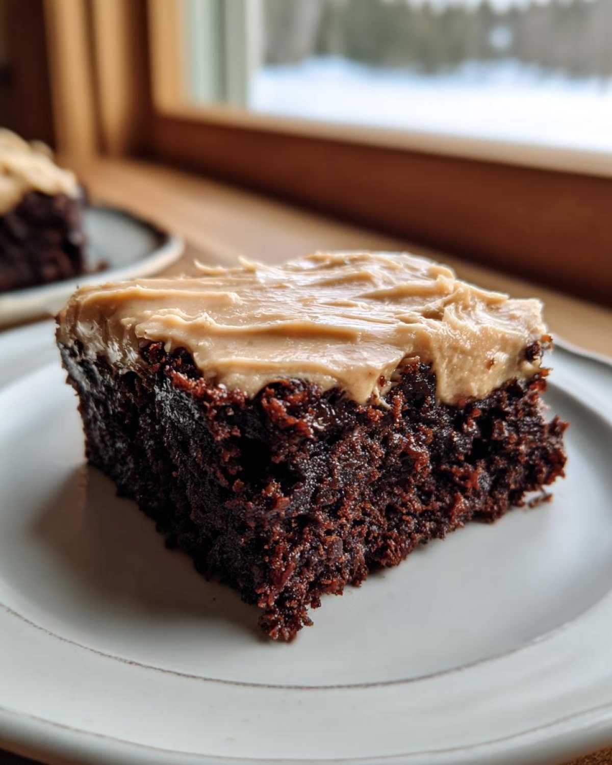 Close-up of a rich, dark chocolate banana bread brownies square topped with creamy peanut butter frosting on a white plate.