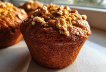 A close-up, sunlit photo of a perfectly baked banana nut muffin topped with chopped walnuts.