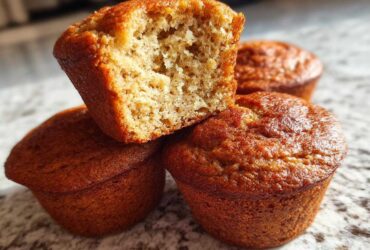 Close-up of four golden brown banana protein muffins, one cut in half showing the moist interior texture.