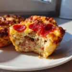 Close-up of a bitten Pizza Muffin showing the savory sausage filling and melted cheese topped with pepperoni.