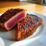 Two halves of a perfectly cooked Blackened Tuna Steak showing a rare, bright pink center and a dark, spicy crust.