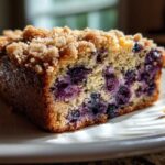 A moist slice of blueberry banana bread featuring a rich crumb topping and visible blueberries throughout the tender crumb.