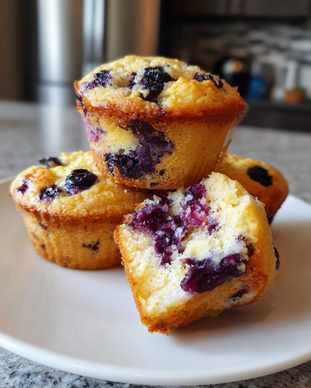 Close-up of three blueberry protein muffins, one cut in half showing the moist interior.
