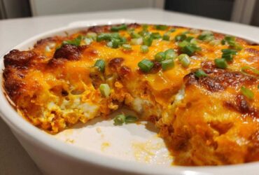 Close-up of a creamy, bubbling Buffalo chicken dip topped with melted orange cheese and green onions.
