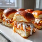 A close-up of juicy buffalo chicken sliders topped with ranch or blue cheese dressing on soft rolls.