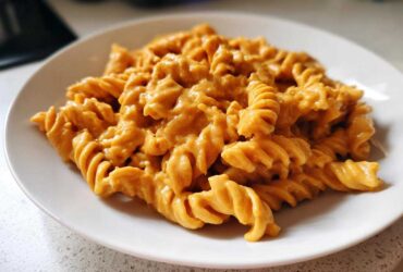 A close-up of fusilli pasta generously coated in a rich, orange butternut squash pasta sauce on a white plate.