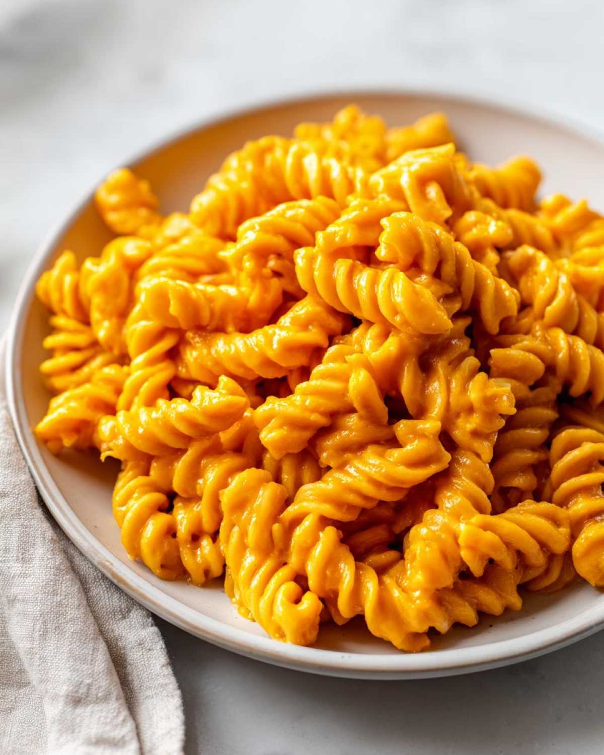 A close-up of rotini pasta coated in a vibrant orange butternut squash pasta sauce served on a white plate.