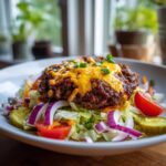 Close-up of a juicy patty topped with melted cheddar cheese in an Amazing cheeseburger bowl over lettuce and toppings.