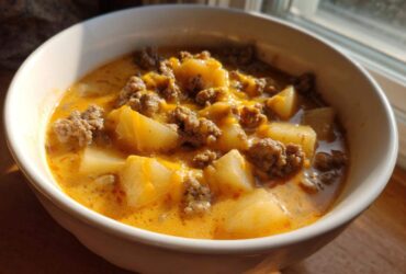Close-up of a white bowl filled with creamy cheeseburger soup featuring chunks of potato and ground beef.