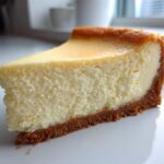 A close-up of a thick, creamy slice of baked cheesecake with a golden-brown top and graham cracker crust, ready for this cheesecake recipe.
