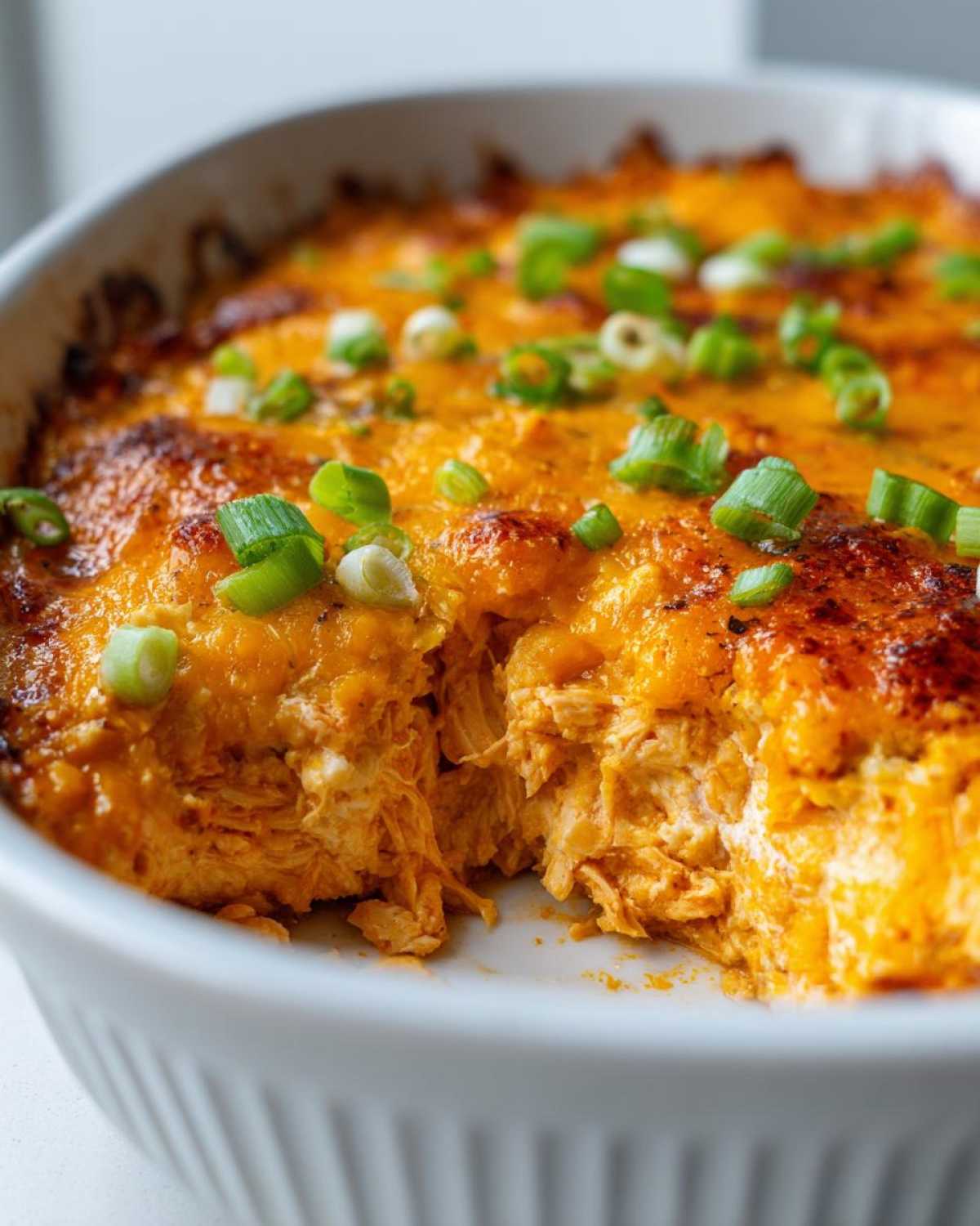 Close-up of hot, cheesy Buffalo chicken dip in a white baking dish, topped with fresh green onions.