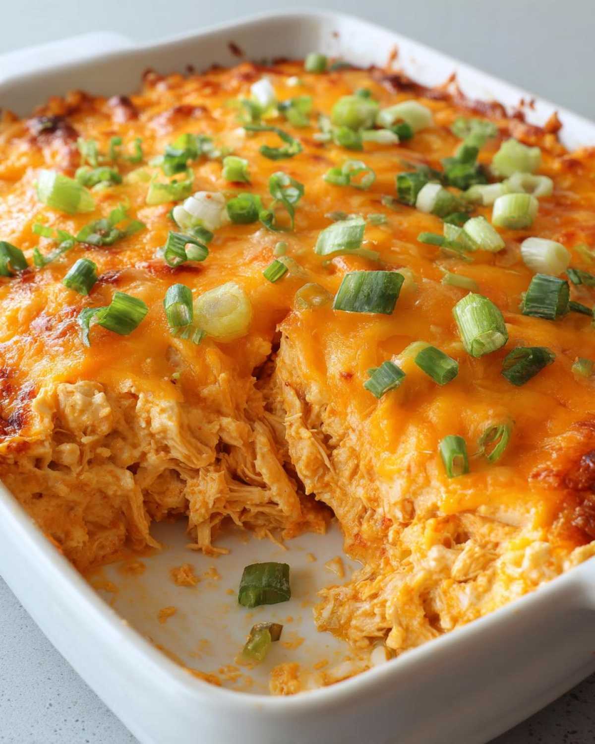 A scoop has been taken out of a hot, cheesy Buffalo chicken dip topped with melted cheddar and chopped green onions.