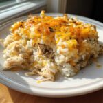 A scoop of cheesy chicken and rice casserole topped with melted cheddar cheese and herbs.