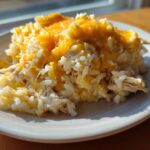 A serving of cheesy chicken and rice casserole topped with melted cheddar cheese on a white plate.