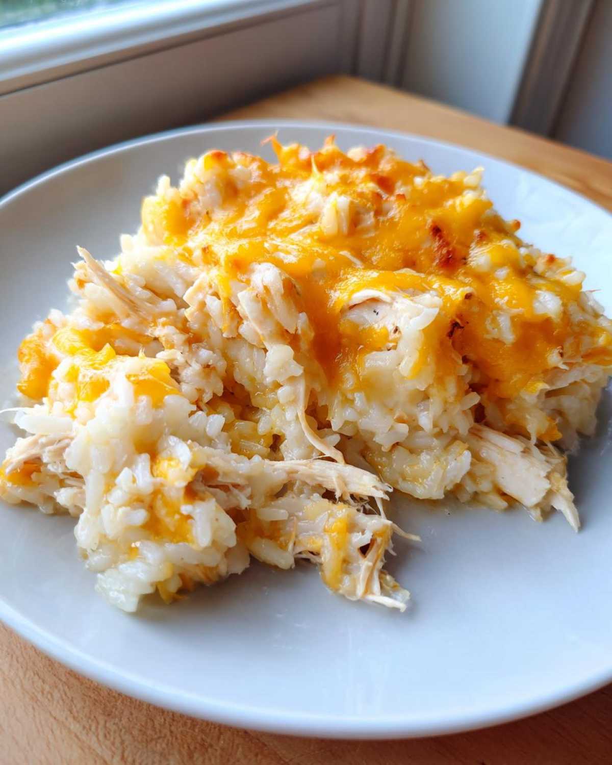 A scoop of cheesy chicken and rice casserole topped with melted cheddar cheese on a light blue plate.