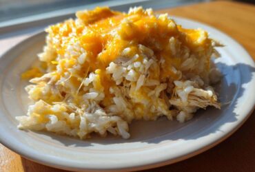A serving of cheesy chicken and rice casserole topped with melted cheddar cheese on a white plate.