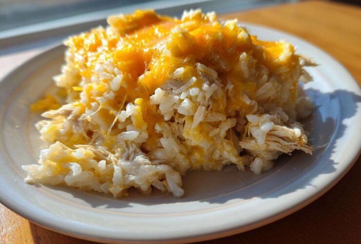 A serving of cheesy chicken and rice casserole topped with melted cheddar cheese on a white plate.
