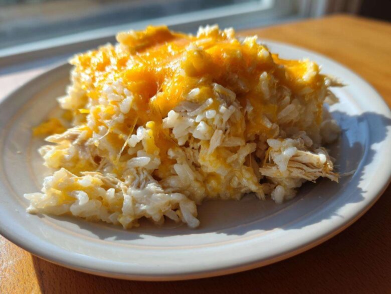 A serving of cheesy chicken and rice casserole topped with melted cheddar cheese on a white plate.