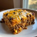 A serving of cheesy mexican rice casserole featuring ground meat, black beans, and corn, topped with melted cheddar.