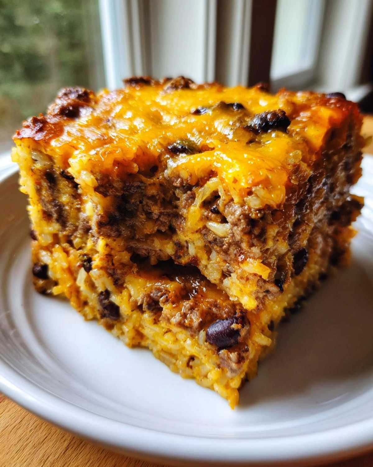 Close-up of a thick, cheesy slice of mexican rice casserole featuring ground beef and black beans.