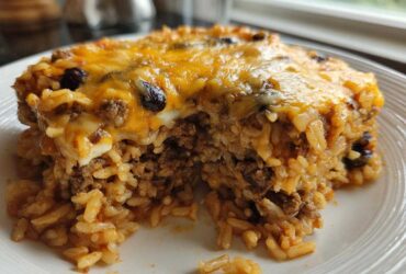 A close-up serving of cheesy mexican rice casserole featuring seasoned ground beef and melted cheddar cheese topping.