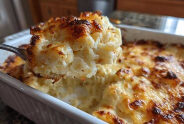 A spoonful of creamy, baked cheesy potato casserole being lifted from the white baking dish.