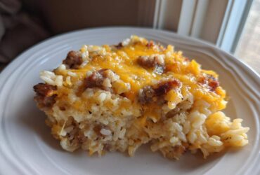 A close-up serving of cheesy sausage and rice casserole topped with melted cheddar cheese.