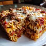 Close-up of a cheesy slice of pizza casserole showing pasta, meat sauce, and melted mozzarella cheese.