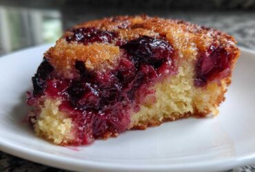 Close-up of a moist slice of cherry dump cake showing the golden cake base and rich, gooey cherry topping.